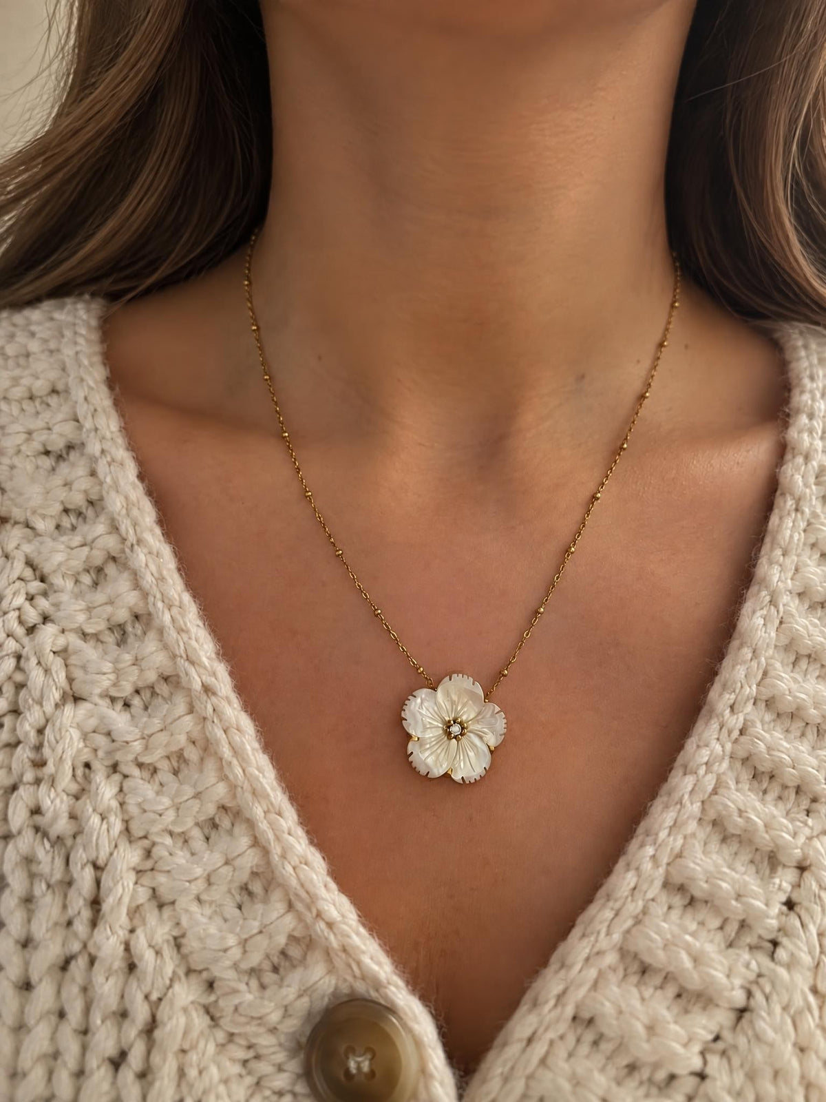 Collier Douceur porté sur un gilet écru en grosse maille, fleur en nacre blanche sur chaîne dorée