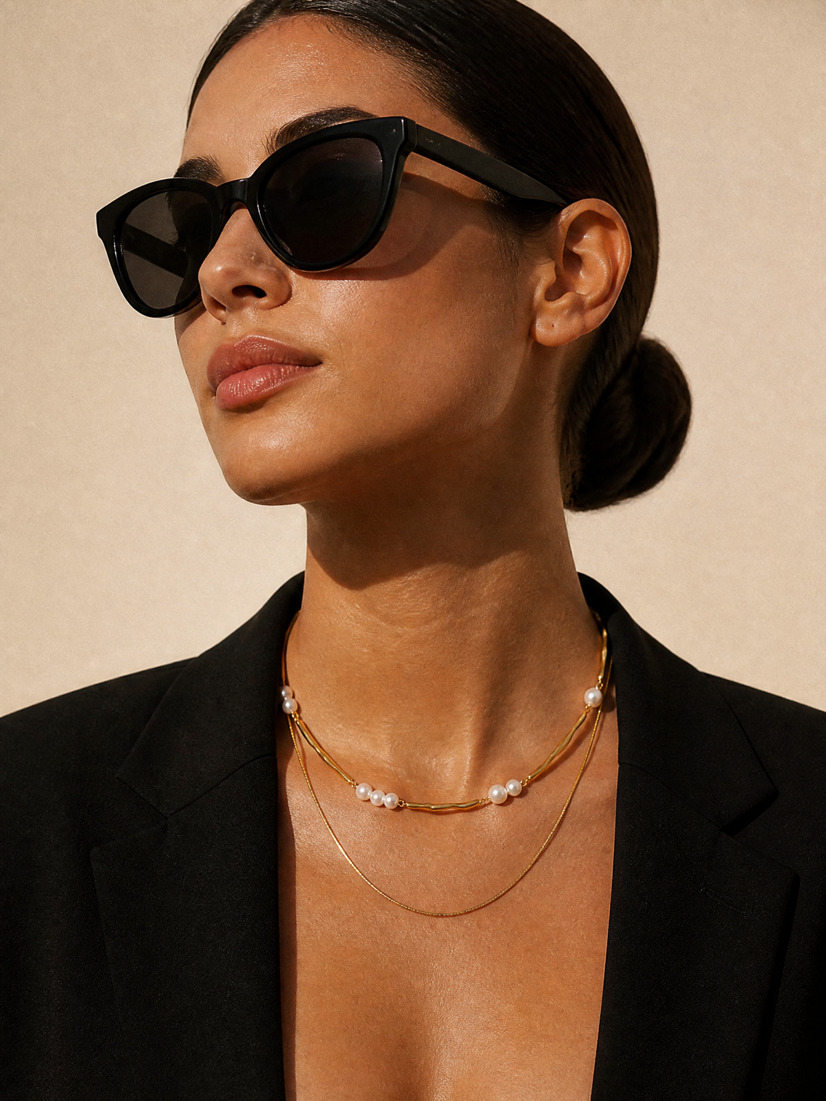 Collier Dune porté, blazer noir et lunettes de soleil : double rang doré et perles nacrées