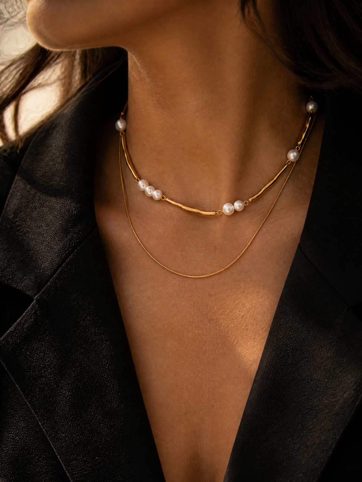 Collier Dune porté sur veste noire : deux rangs dorés, barrette ondulée et perles nacrées