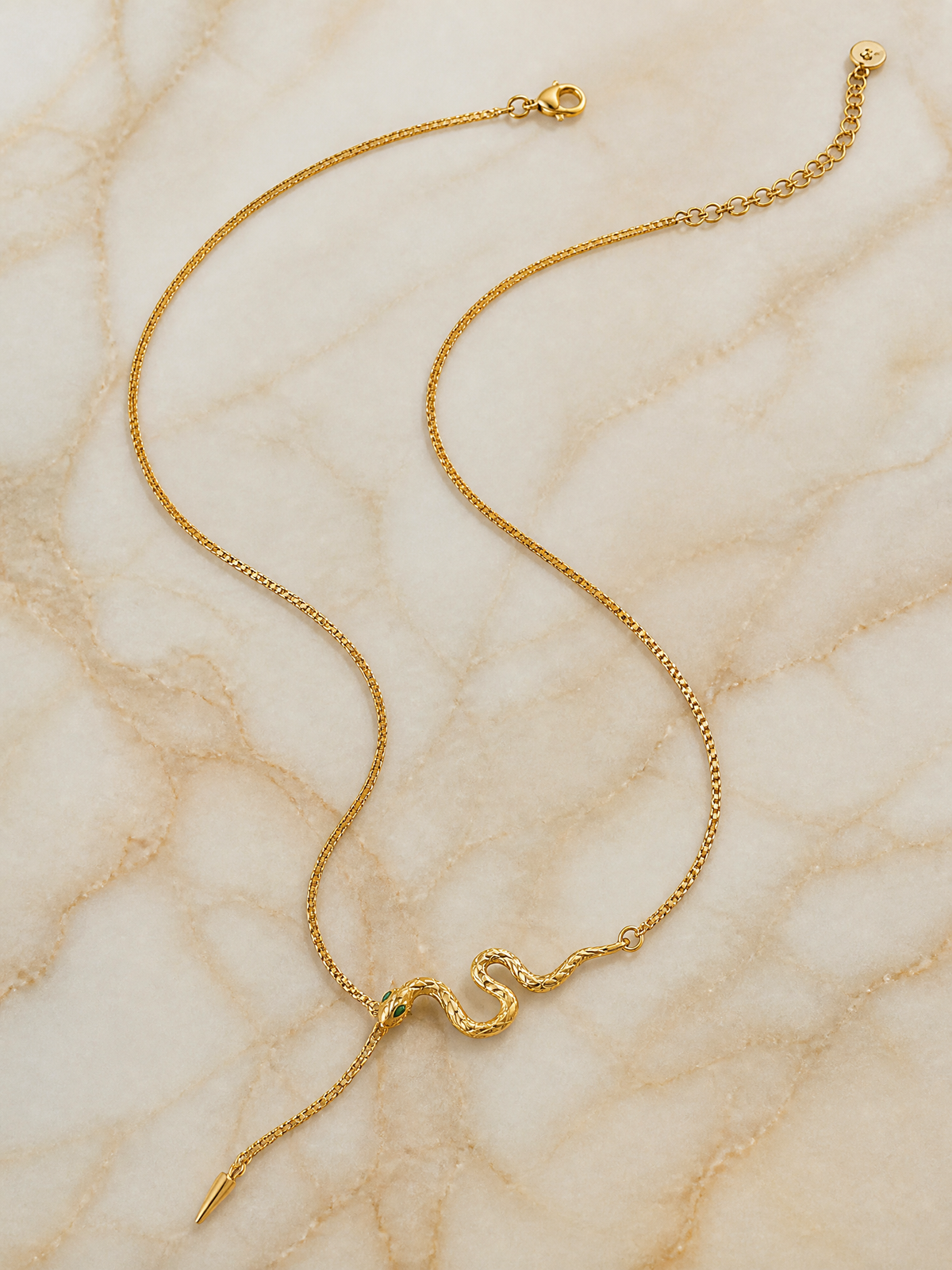 Collier Serpentina à plat sur marbre crème : chaîne fine dorée, serpent et pointe effilée