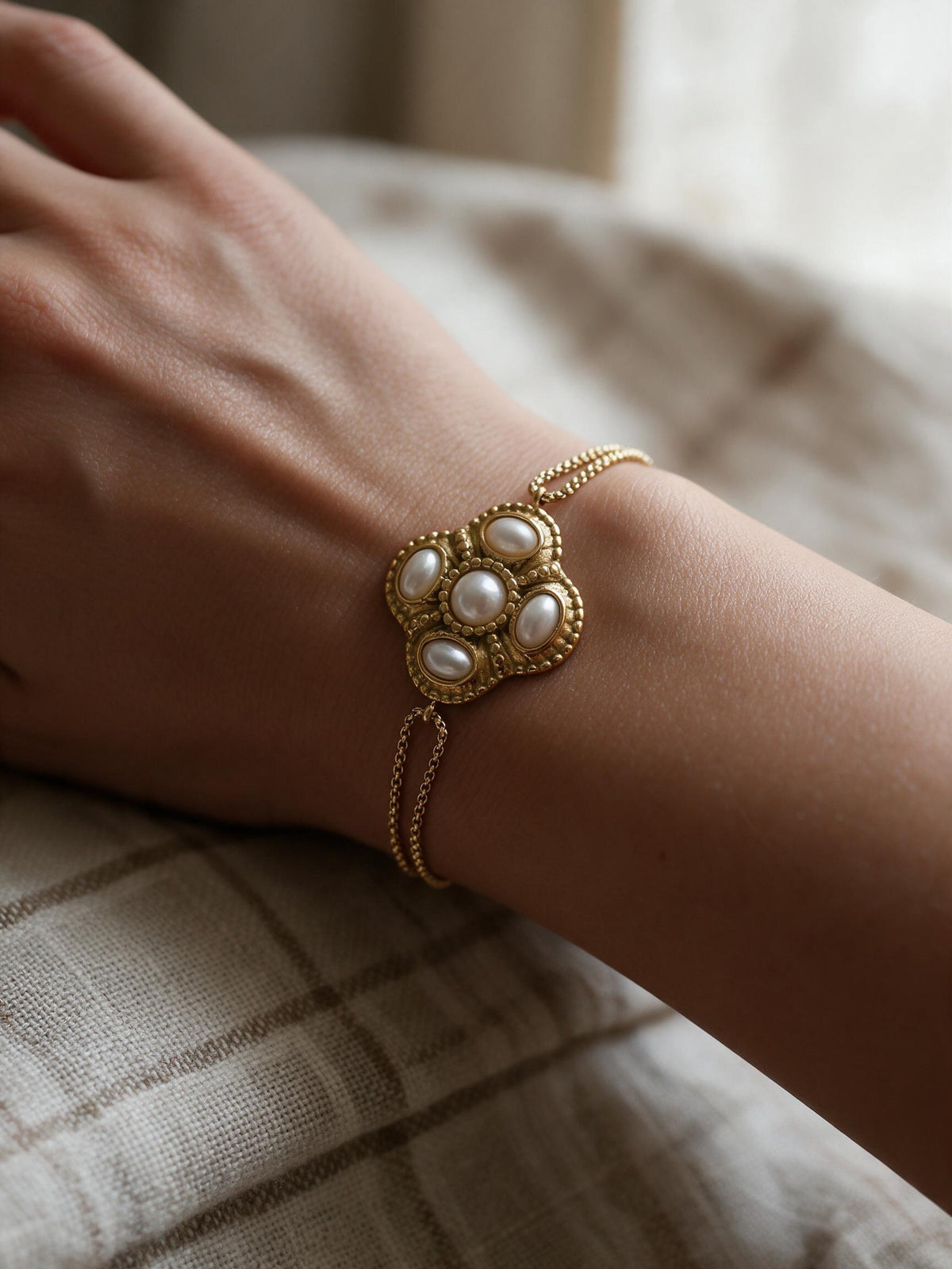 Bracelet Médina perles nacrées porté au poignet – rosace dorée à cinq cabochons crème sur double chaîne