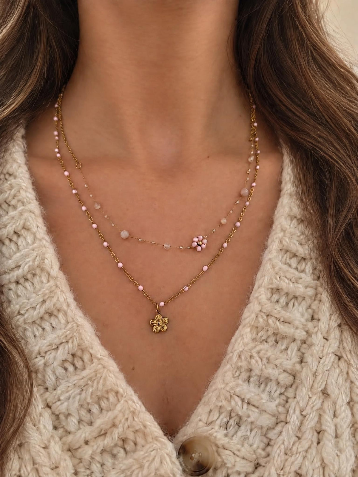 Collier Aurora porté sur un gilet écru, double chaîne dorée à perles roses