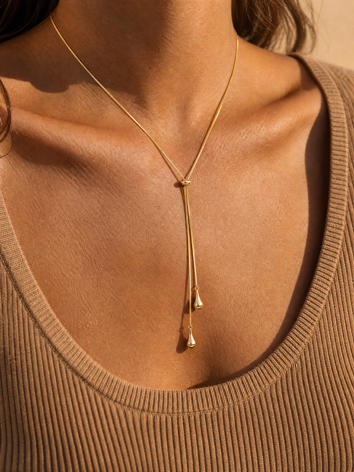 Collier Thaïs cravate en maille serpent dorée porté sur un pull camel, deux gouttes en V