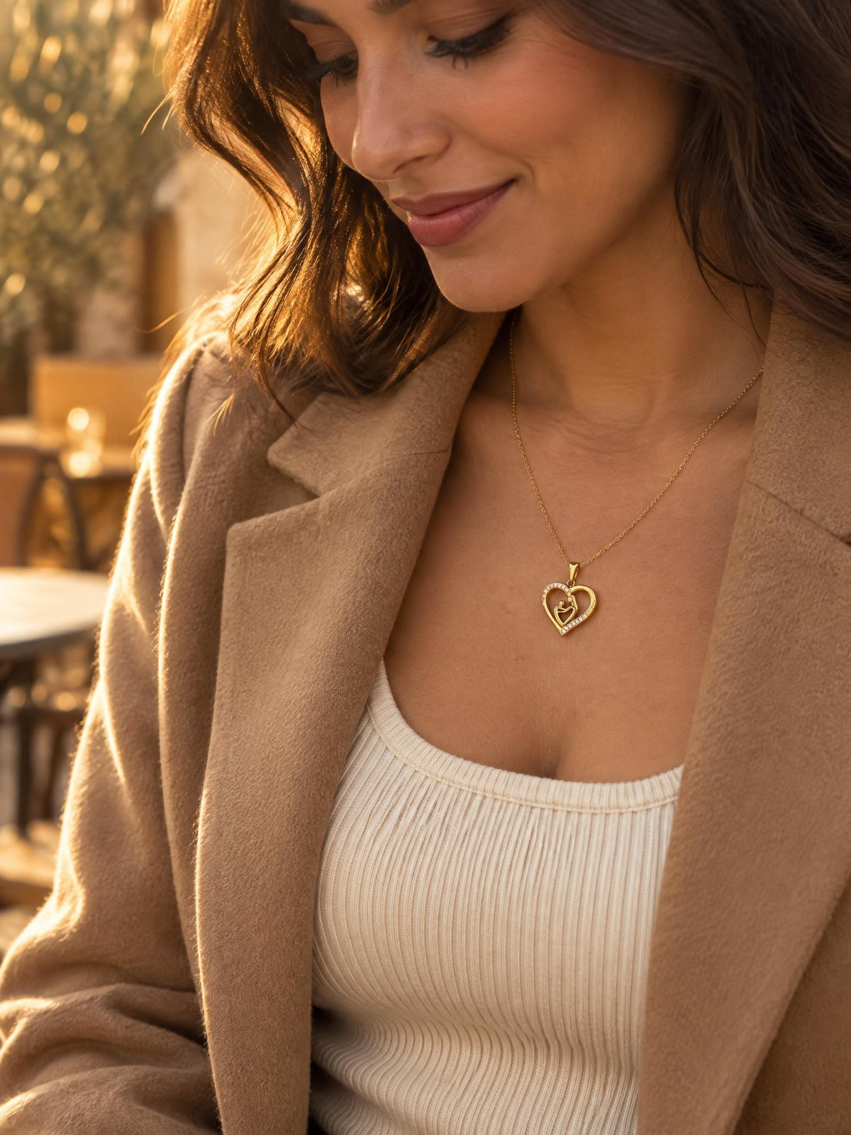 Femme en manteau camel portant le collier Maélie, pendentif cœur doré mère-enfant, lumière d'automne
