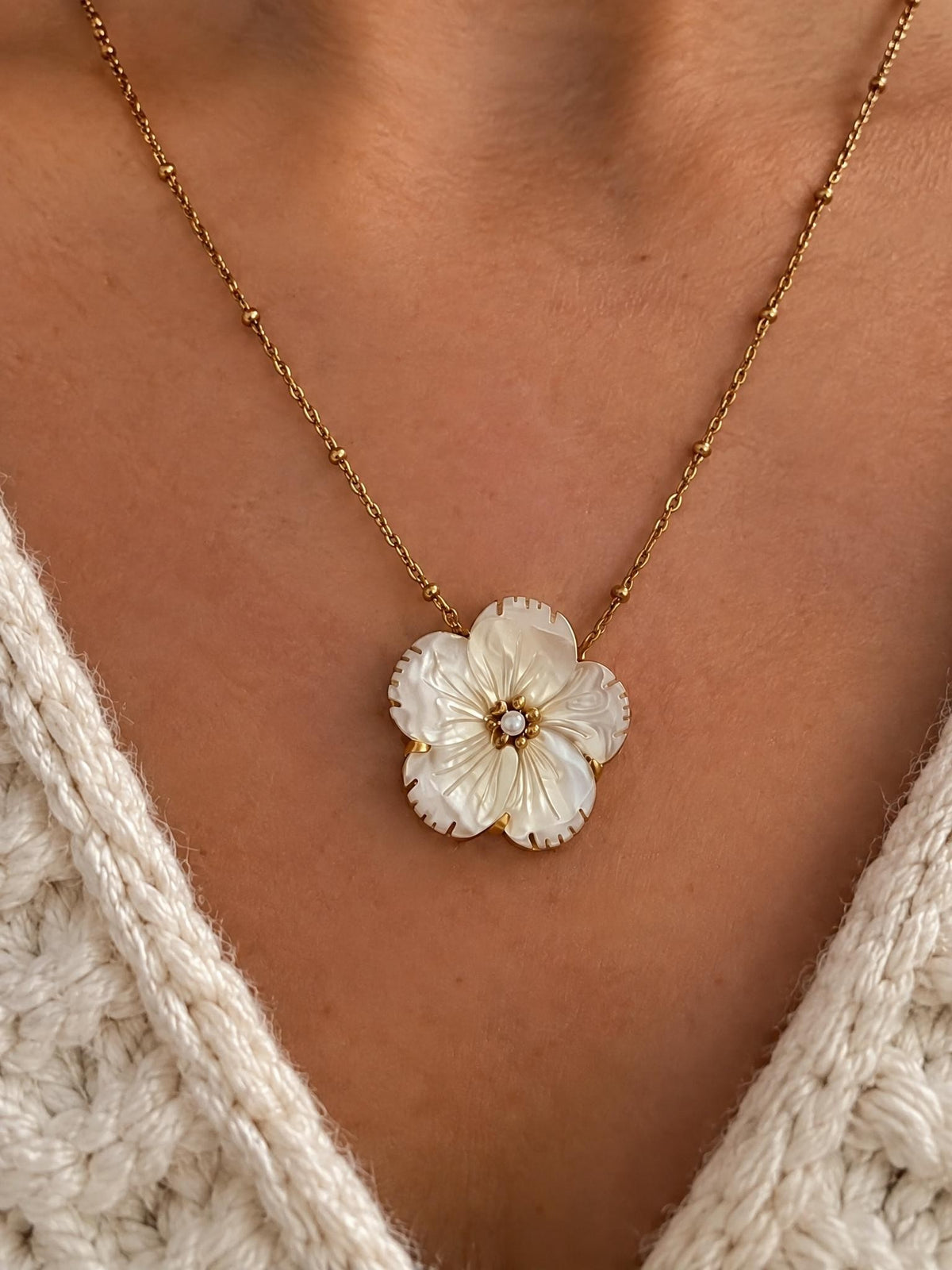 Gros plan sur la fleur en nacre blanche sculptée du Collier Douceur et sa chaîne dorée à billes