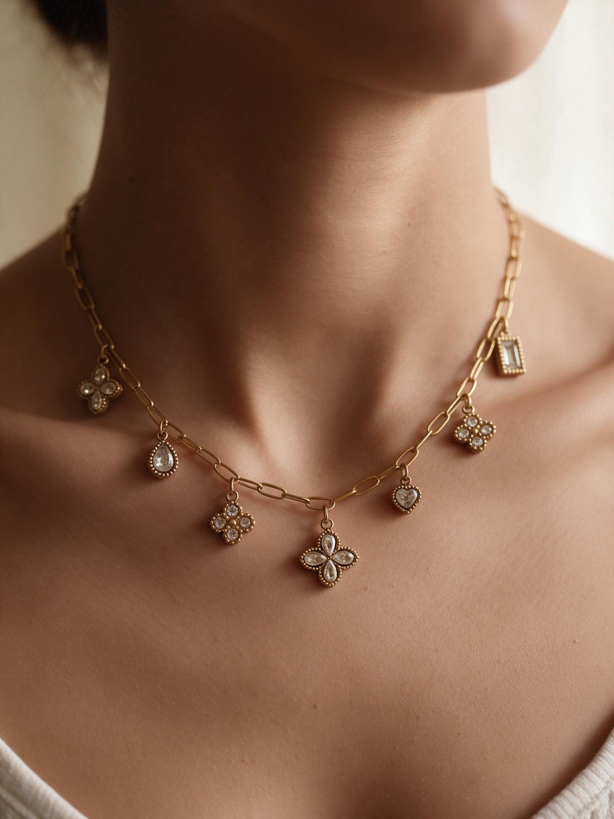 Collier Anela porté en gros plan – sept pendentifs sertis, quatre-feuilles, goutte, cœur et rectangle, sur chaîne à maillons trombone dorée